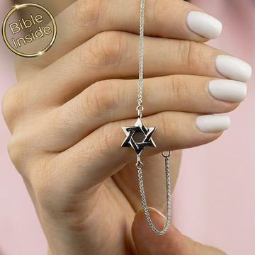 צמיד תנך עם מגן דוד בגוון כסף, מוחזק ביד לצד שרשרת דקה