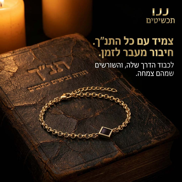 צמיד תנ"ך לאישה בגוון זהב מונח על ספר תנ״ך לצד נרות דולקים